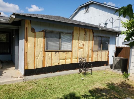 A house with a wooden wall and a chair outside.