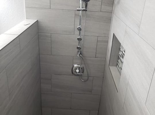 A modern shower with tiled floor and wall.