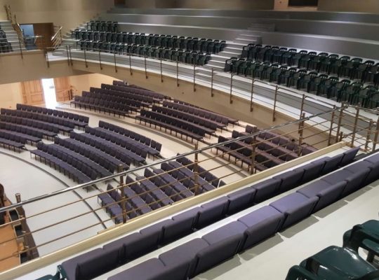 A large auditorium with green seats and a stage.