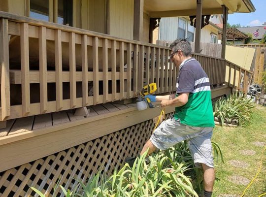 A man using a power tool to paint a wooden porch.